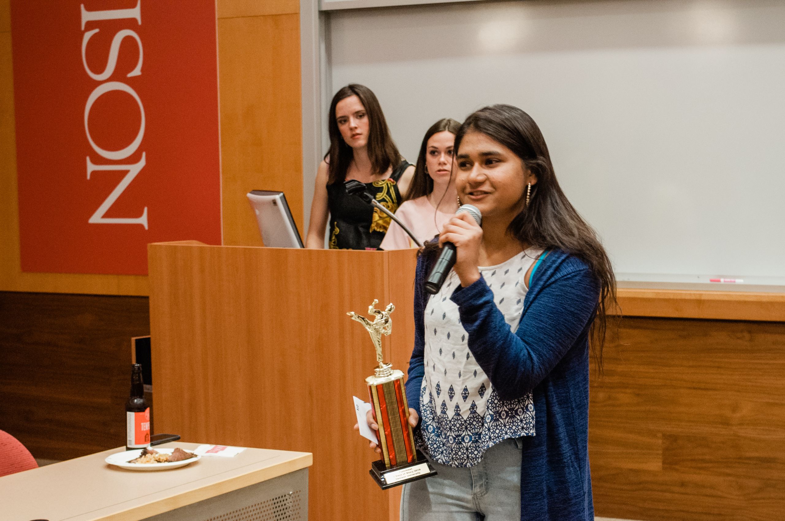 A woman stands with a trophy speaking into a microphone