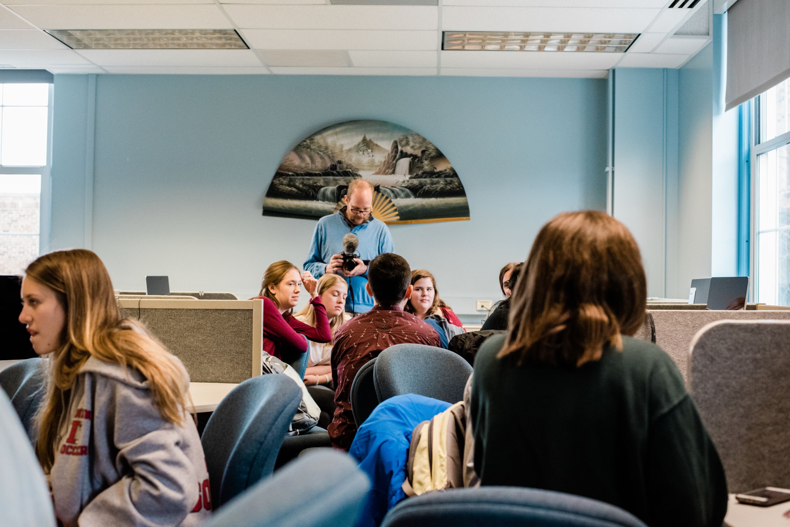 Students sit in a lab with Doug Swift recording video in the background.