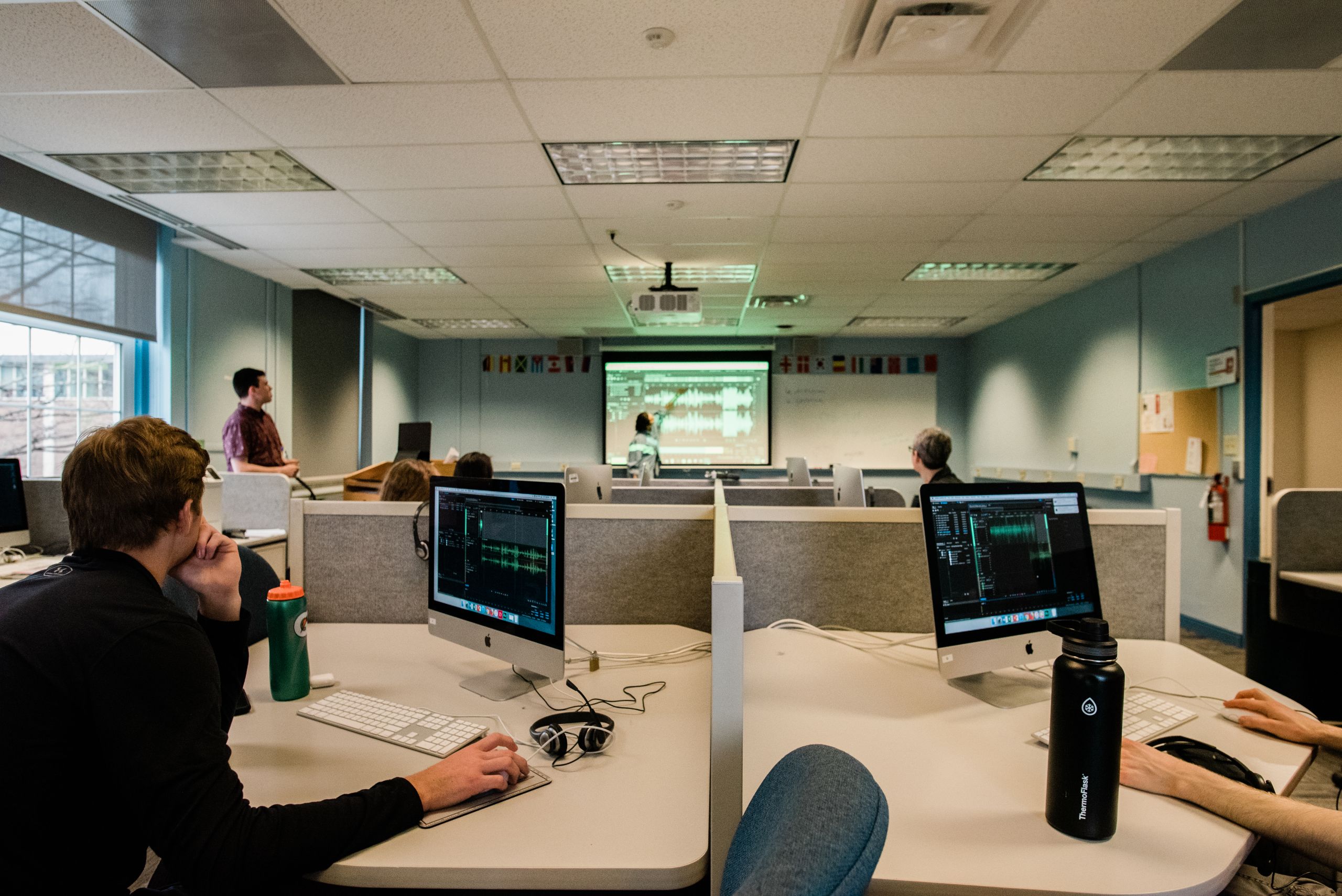 Students sit at lab computers while journalists lead a workshop in the front of a room.