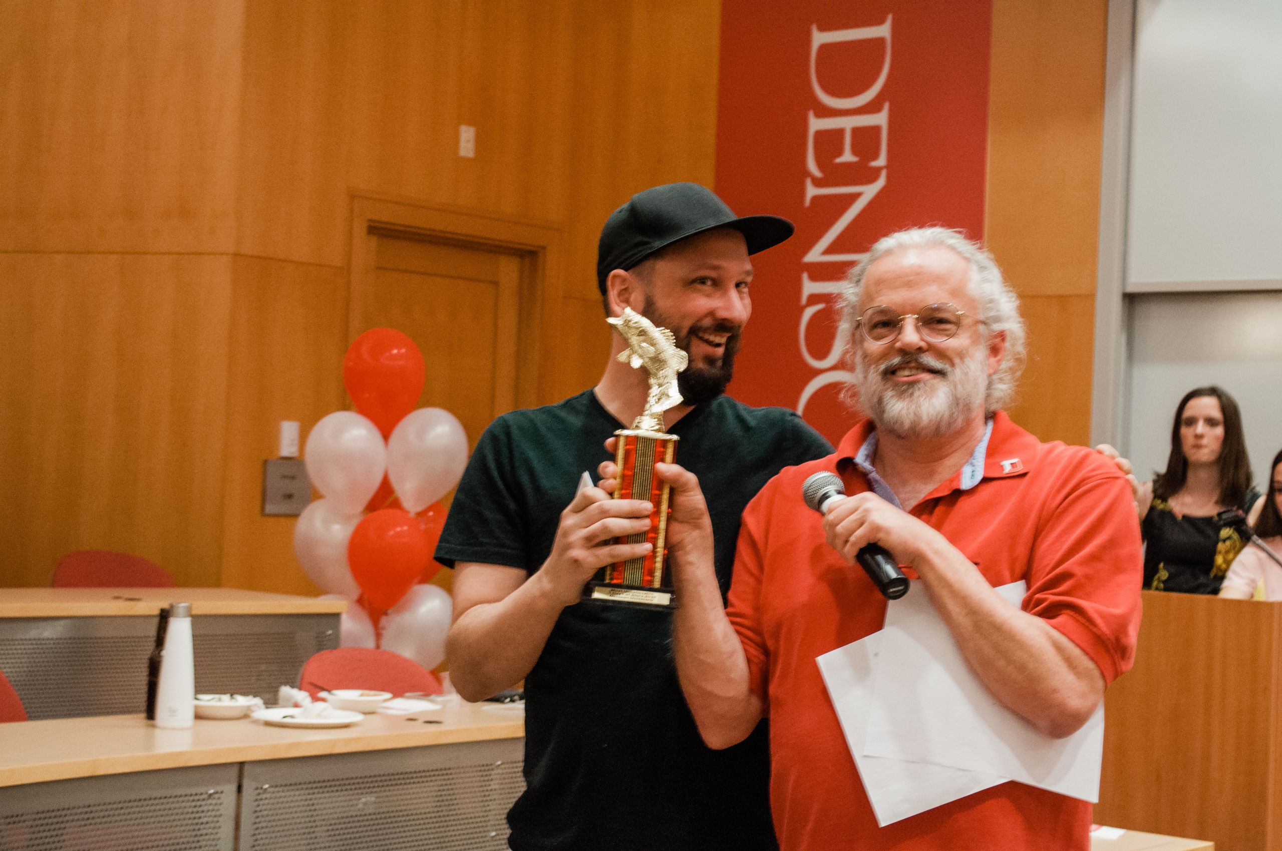 Two men stand next to each other holding a trophy.