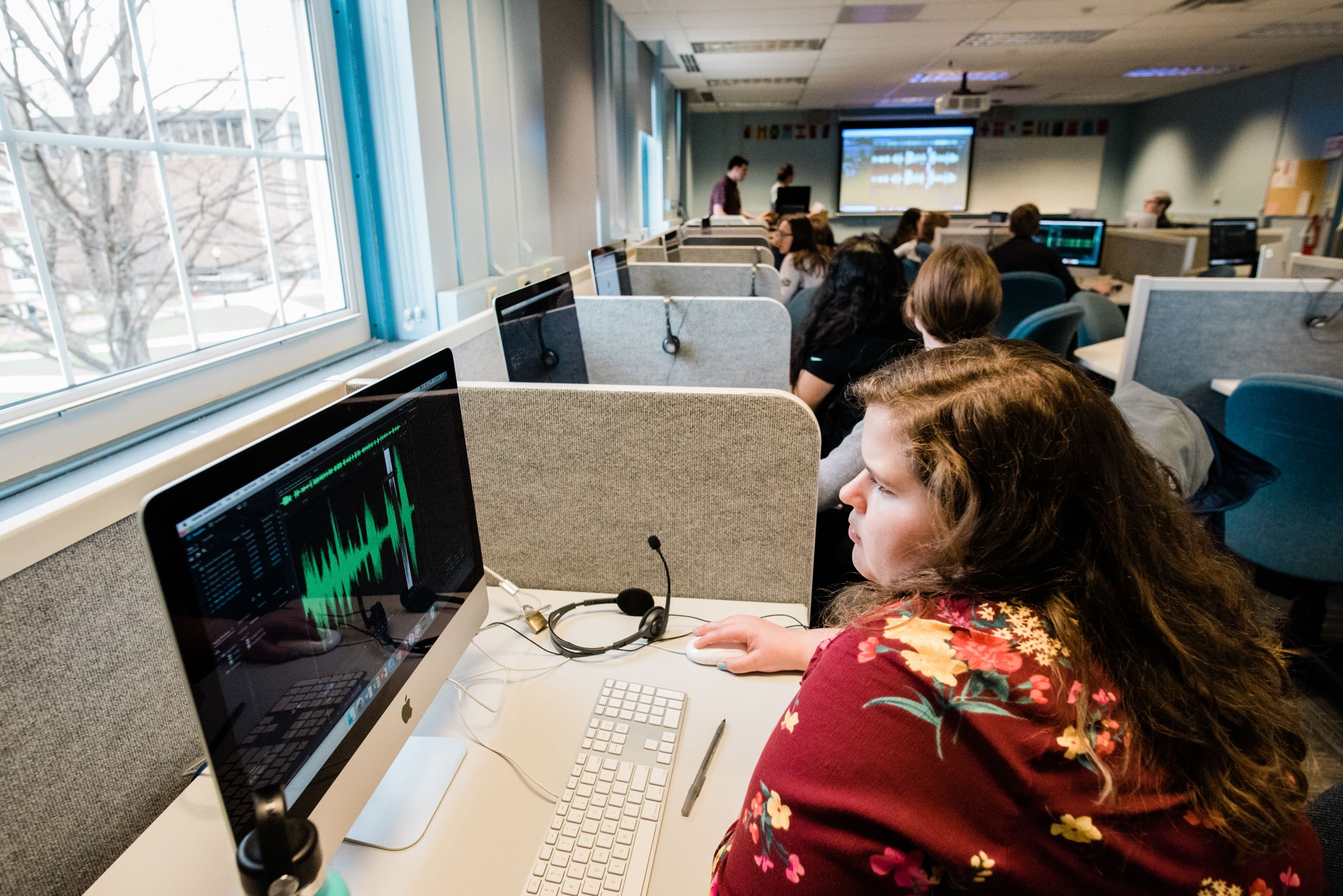 Student sitting in front of a computer working on audio files.